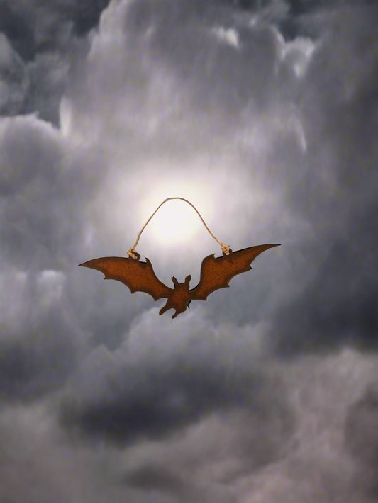 A metal ornament in the shape of a bat with a brownish-gold color, hanging from a a jute cord.