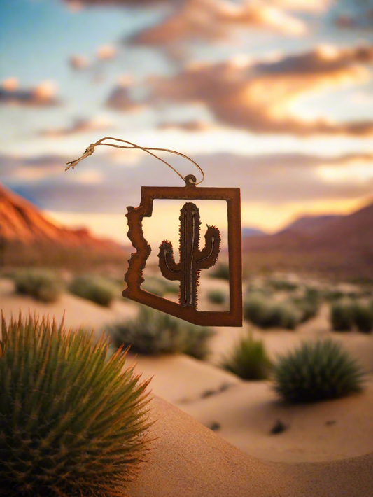 Decorative ornament shaped like Arizona with a cactus silhouette against a desert sunset.