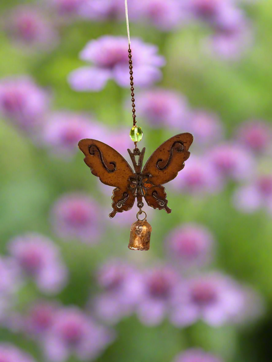 Butterfly-shaped ornament with a bell hanging against a blurred background of pink flowers.