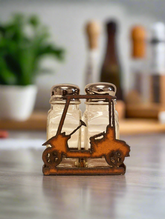 A decorative golf cart-shaped salt and pepper shaker holder made of metal with a rustic finish, placed against a wooden background.